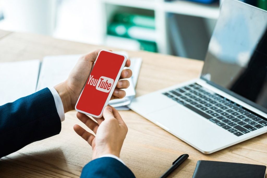 Businessman holding a phone displaying the YouTube logo at his desk